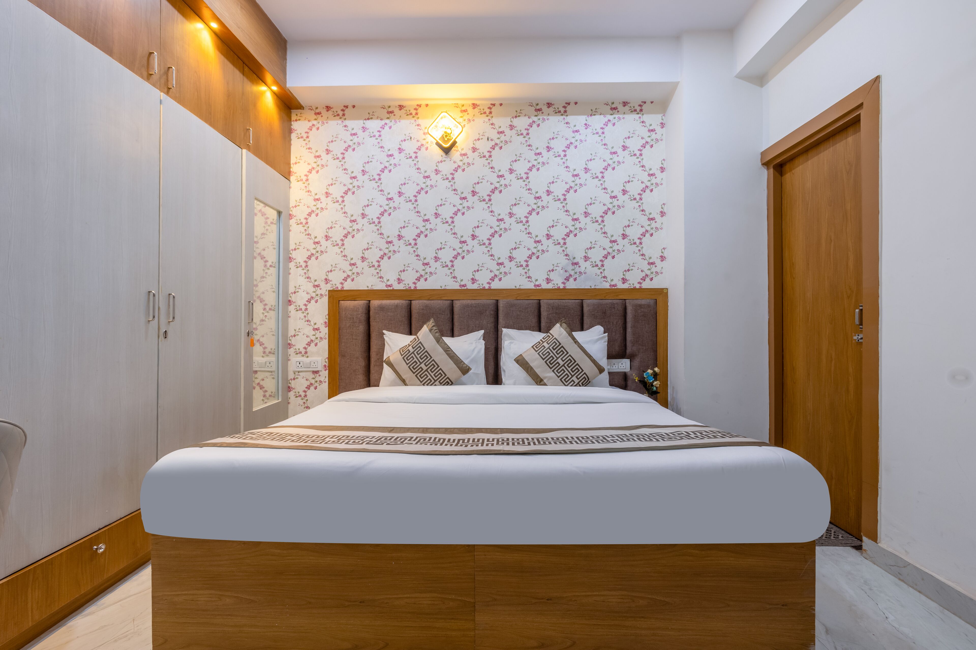 Quarto com cama, guarda-roupa de madeira e luminária na parede.