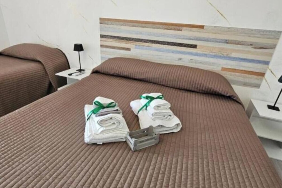 A hotel room with a large bed, two pillows, a bedside table with a lamp, and a wall with a striped pattern.