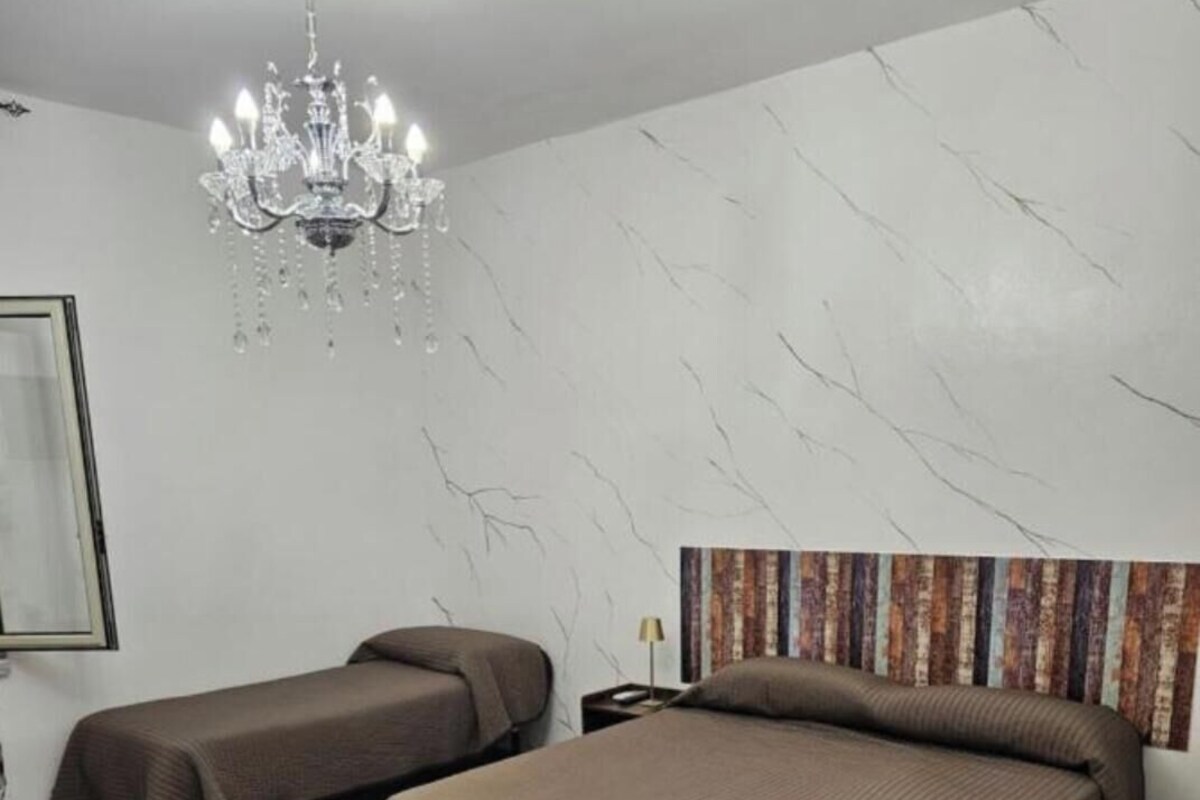 A hotel room with two beds, a chandelier, a marble-patterned wall, and a framed picture.