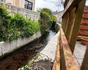 A narrow water channel with a concrete wall on one side and a wooden fence on the other.