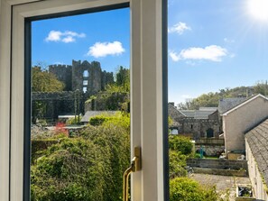 Blick durch ein Fenster auf eine Burgruine, einen Garten und ein Gebäude mit einem geneigten Dach.