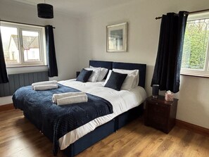 A neatly made bed with white and navy bedding, a bedside table with a lamp, and a window with curtains.