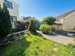 A garden with a stone wall, a blue gate, and a pathway leading to a building.