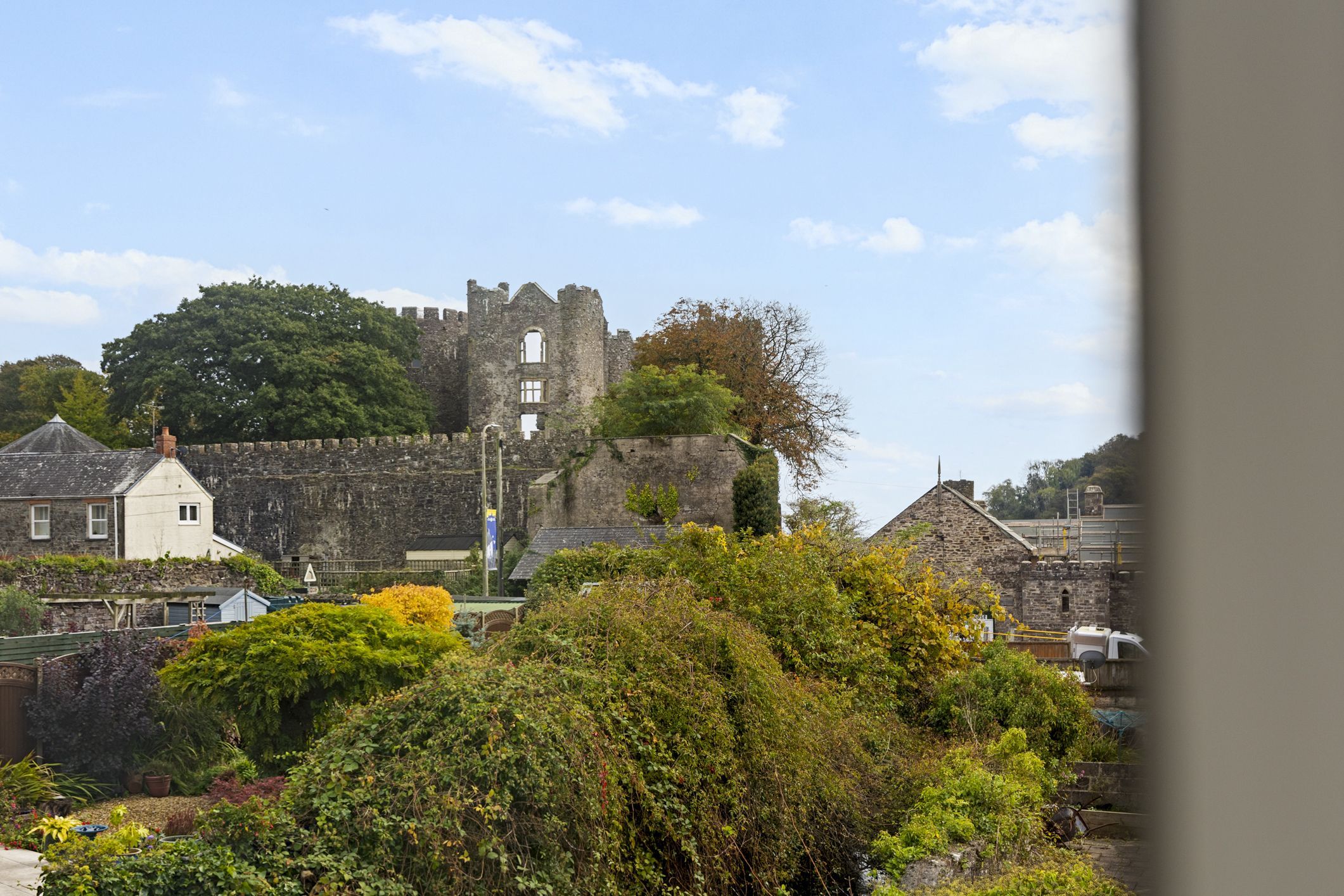 A historic stone castle with a moat, surrounded by lush greenery and modern buildings.