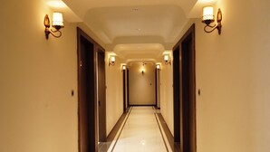 A hotel hallway with a marble floor, wooden doors, and wall-mounted lights. - HOTEL LEELA INN (Asnawar)