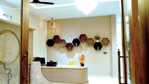 A reception area with a curved reception desk, a ceiling fan, a chandelier, and a wall-mounted hexagonal shelf unit with potted plants. - HOTEL LEELA INN (Asnawar)