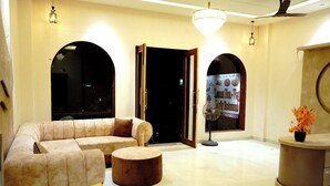 A modern lobby with a sofa, ottoman, fan, and a circular table with a potted plant. - HOTEL LEELA INN (Asnawar)
