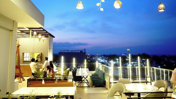 An outdoor dining area with tables and chairs, a view of the cityscape, and hanging lights. - HOTEL LEELA INN (Asnawar)