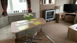 A compact living space with a sofa, a dining table, a television, and a small kitchenette. - Berwick Holiday Park - Holiday Accommodation 4088 (Berwick-upon-Tweed)