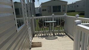 A wooden deck with a white railing, a table with chairs, and a view of adjacent mobile homes. - Berwick Holiday Park - Holiday Accommodation 4088 (Berwick-upon-Tweed)
