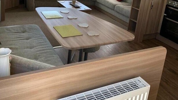 A cozy RV interior with a sofa, table, and kitchenette. - Berwick Holiday Park - Holiday Accommodation 4088 (Berwick-upon-Tweed)