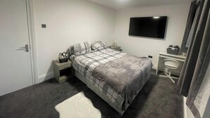 A bedroom with a bed, bedside table, TV, and a small desk with a chair. - House Sleeps 9 With Garden and Parking (Bradford)