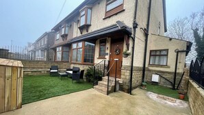 A two-story house with a front porch, a small garden, and a wooden shed. - House Sleeps 9 With Garden and Parking (Bradford)