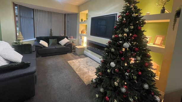 A modern living room with a large flat-screen TV, a dark-colored sofa, a Christmas tree, and a fireplace. - House Sleeps 9 With Garden and Parking (Bradford)