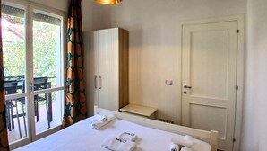 Ein Hotelzimmer mit Bett, Schrank, kleinem Tisch, einer Tür und einem Fenster mit Vorhängen.