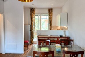 Ein Essbereich mit Tisch und Stühlen, ein Küchenbereich mit Kühlschrank und ein Fenster mit Vorhängen.