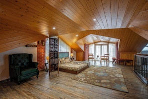 Un dormitorio estilo loft con techo de madera, una cama, un sillón verde y una zona de comedor con sillas.