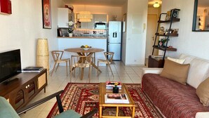 Uma sala de estar com sofá, mesa de centro, televisão e um espaço de jantar com cadeiras e mesa.