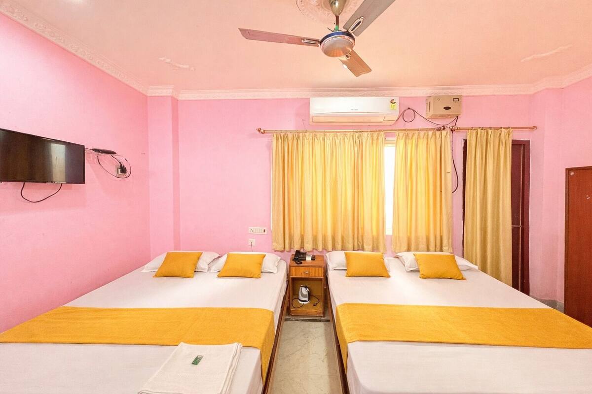 Une chambre d’hôtel avec deux lits, un ventilateur de plafond, un appareil de climatisation et un téléviseur fixé au mur.