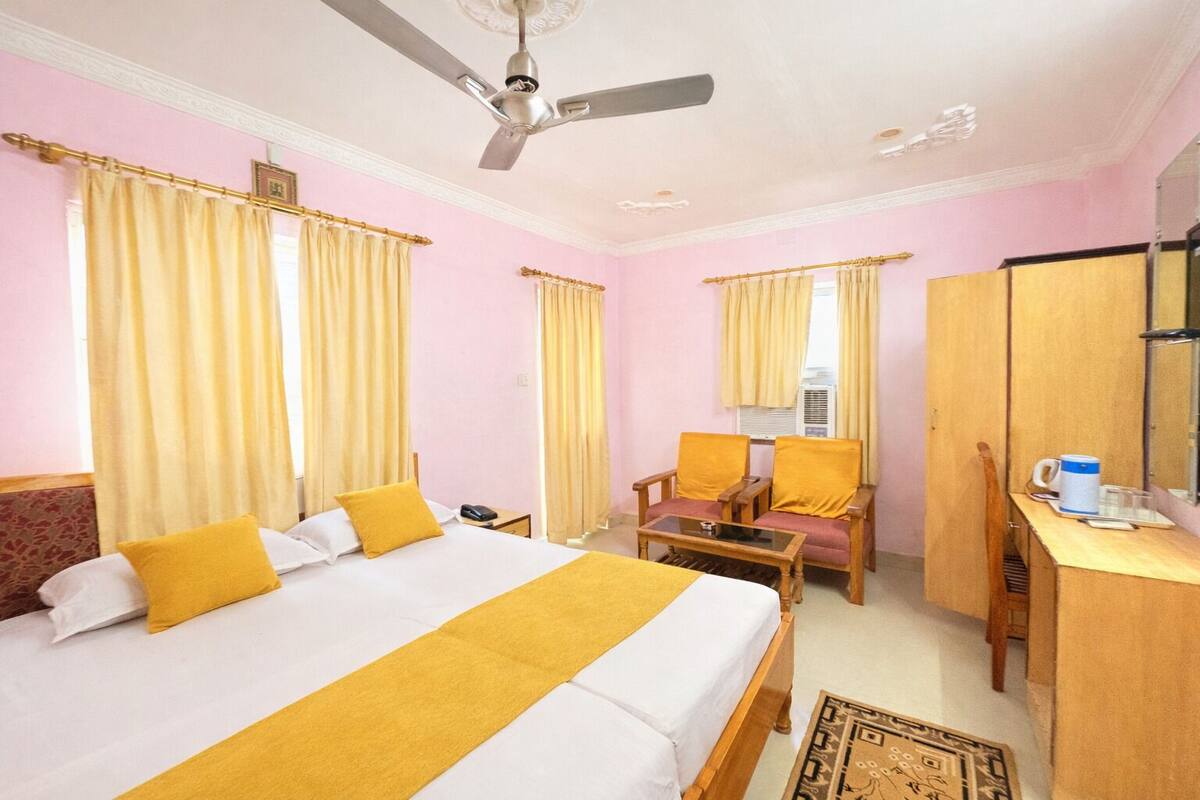 Une chambre d’hôtel avec un lit, un bureau, une chaise, un ventilateur de plafond et des rideaux.