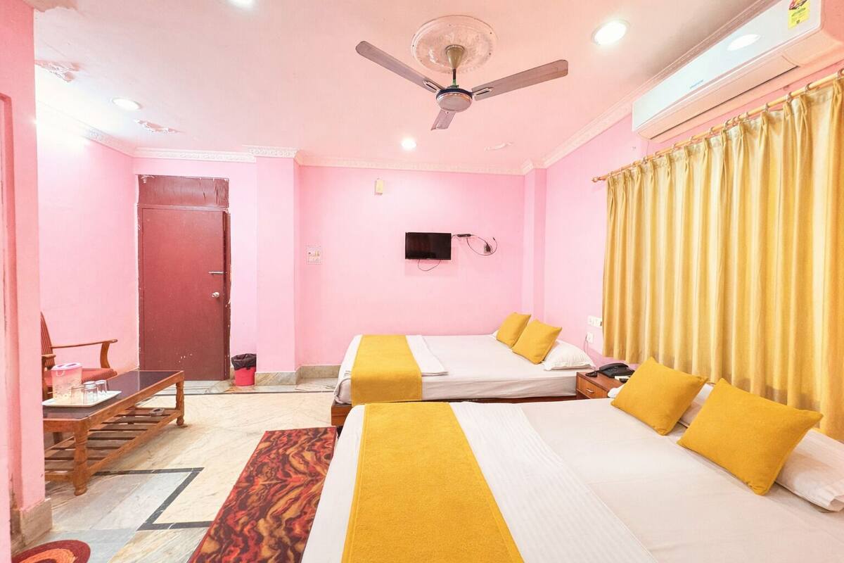 Une chambre d’hôtel avec deux lits, un ventilateur de plafond, une télévision et une fenêtre avec des rideaux.