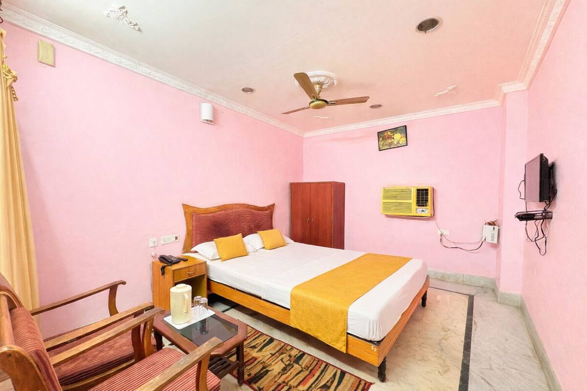 Une chambre rose avec un lit, un bureau, une chaise, un ventilateur de plafond et un téléviseur.