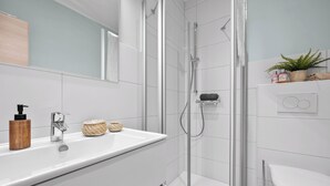 A modern bathroom with a glass-enclosed shower, a white sink with a wooden soap dispenser, and a mirror above the sink. - “Apartment Amrum” in the heart of Büsum with balcony, centrally located and clos (Büsum)