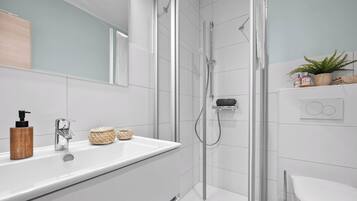 Un baño moderno con ducha envuelta en vidrio, un lavabo blanco con dispensador de jabón de madera y un espejo sobre el lavabo.