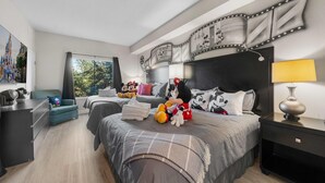 Ein modernes Schlafzimmer mit einem großen Bett, einem Schreibtisch und einem Stuhl. Auf dem Bett liegen Mickey Mouse Kuscheltiere.