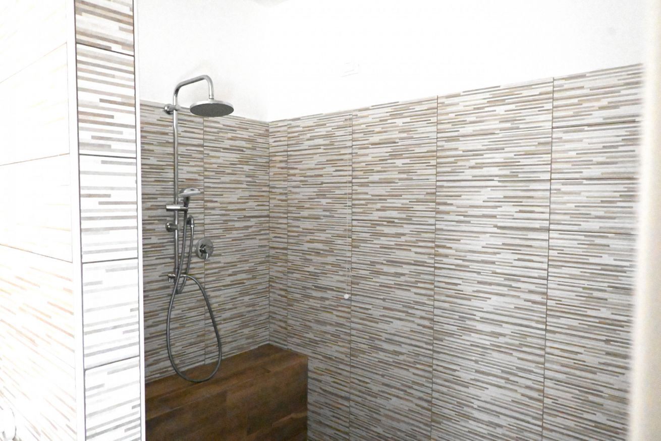 A shower with a modern design, a wooden floor, and a tiled wall with a horizontal pattern.