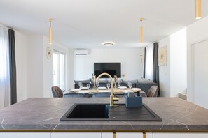 A modern kitchen with a marble countertop, a gold faucet, and a dining area with a sofa and table set for four. - Villa IviCasa with pool (Murvica)