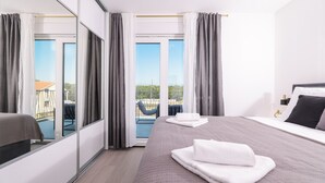 A modern hotel room with a large bed, a balcony with a chair, and a view of the landscape. - Villa IviCasa with pool (Murvica)