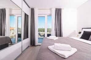 A modern hotel room with a large bed, a balcony with a chair, and a view of the landscape. - Villa IviCasa with pool (Murvica)