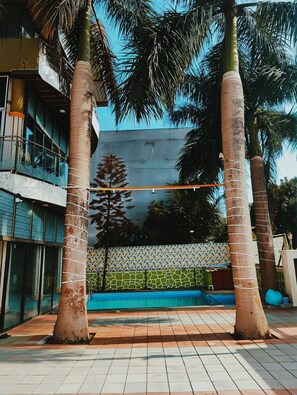 A pool area with tiled flooring, palm trees, and a building with glass windows and a tiled wall.