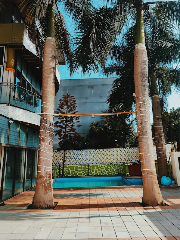 A pool area with tiled flooring, palm trees, and a building with glass windows and a tiled wall.