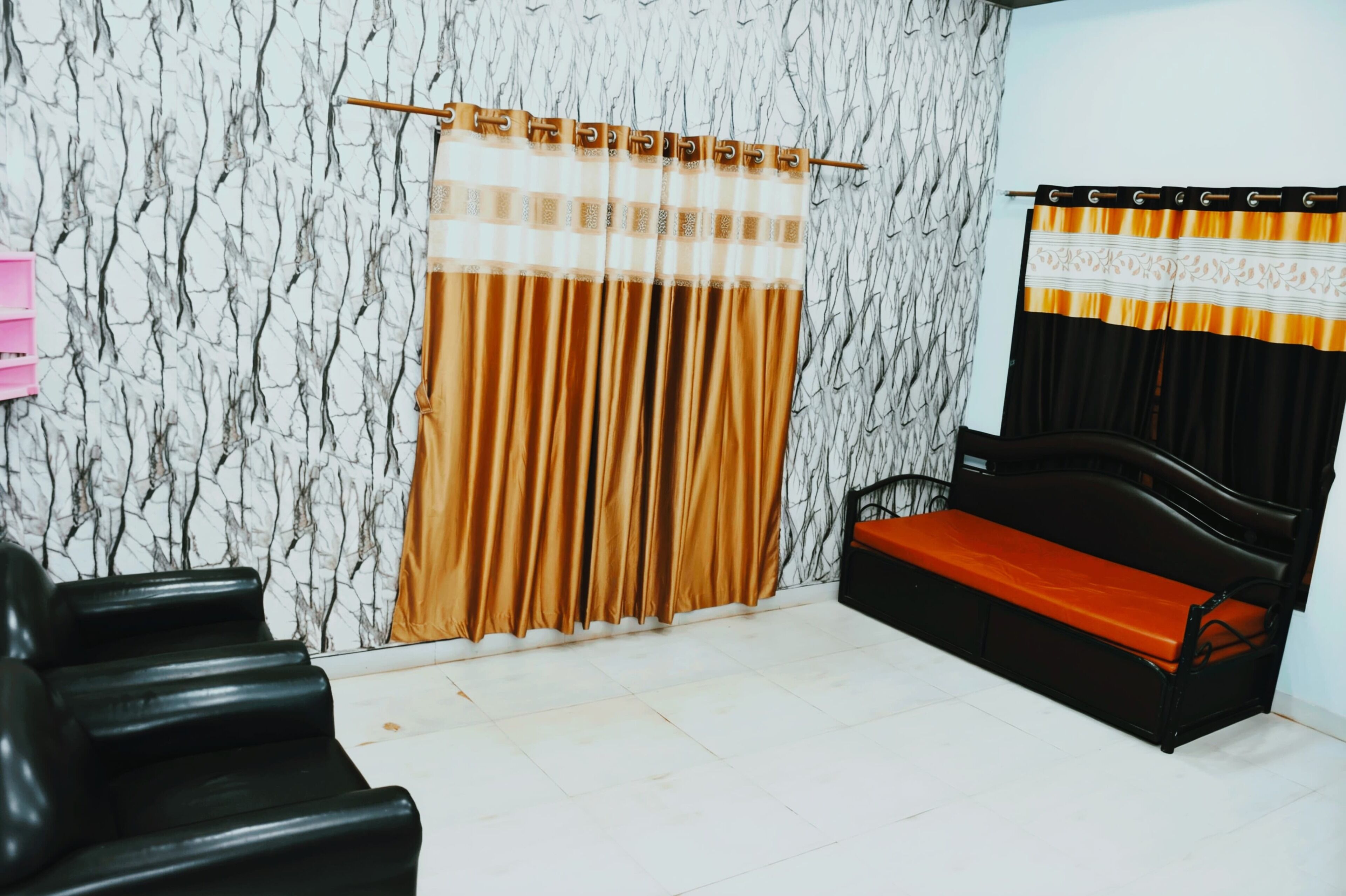 A room with a marble-patterned wall, a sofa with an orange cushion, a black chair, and a curtain with a patterned top.