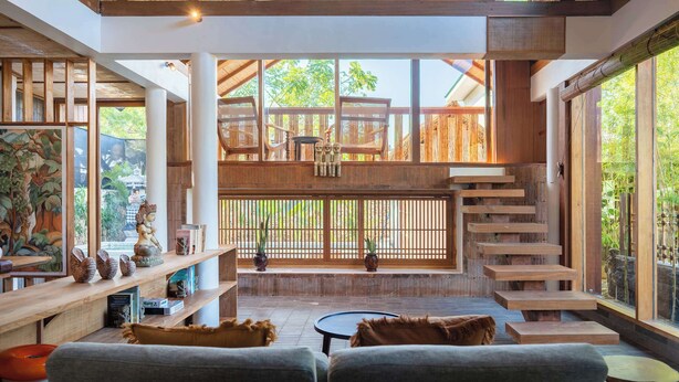 Un interior amplio con escalera de madera, zona de estar con sofás y ventanas grandes que ofrecen vistas al exterior.