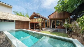 Una casa moderna con piscina, terraza de madera y techo de paja.