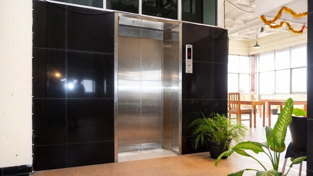 An elevator in a lobby with black walls, potted plants, and a wooden table. - Kailani Inn (Medan)