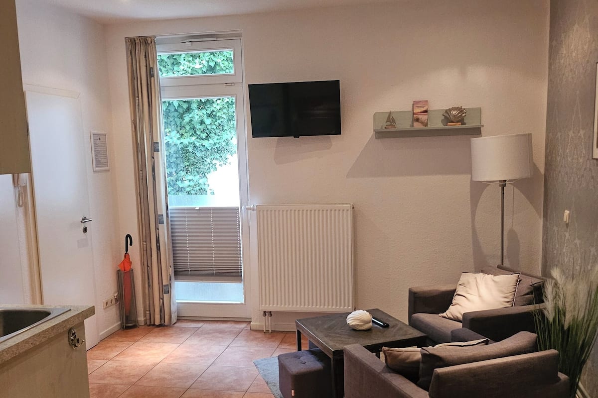 Un salon avec un canapé, un téléviseur, un radiateur et une fenêtre avec des rideaux.