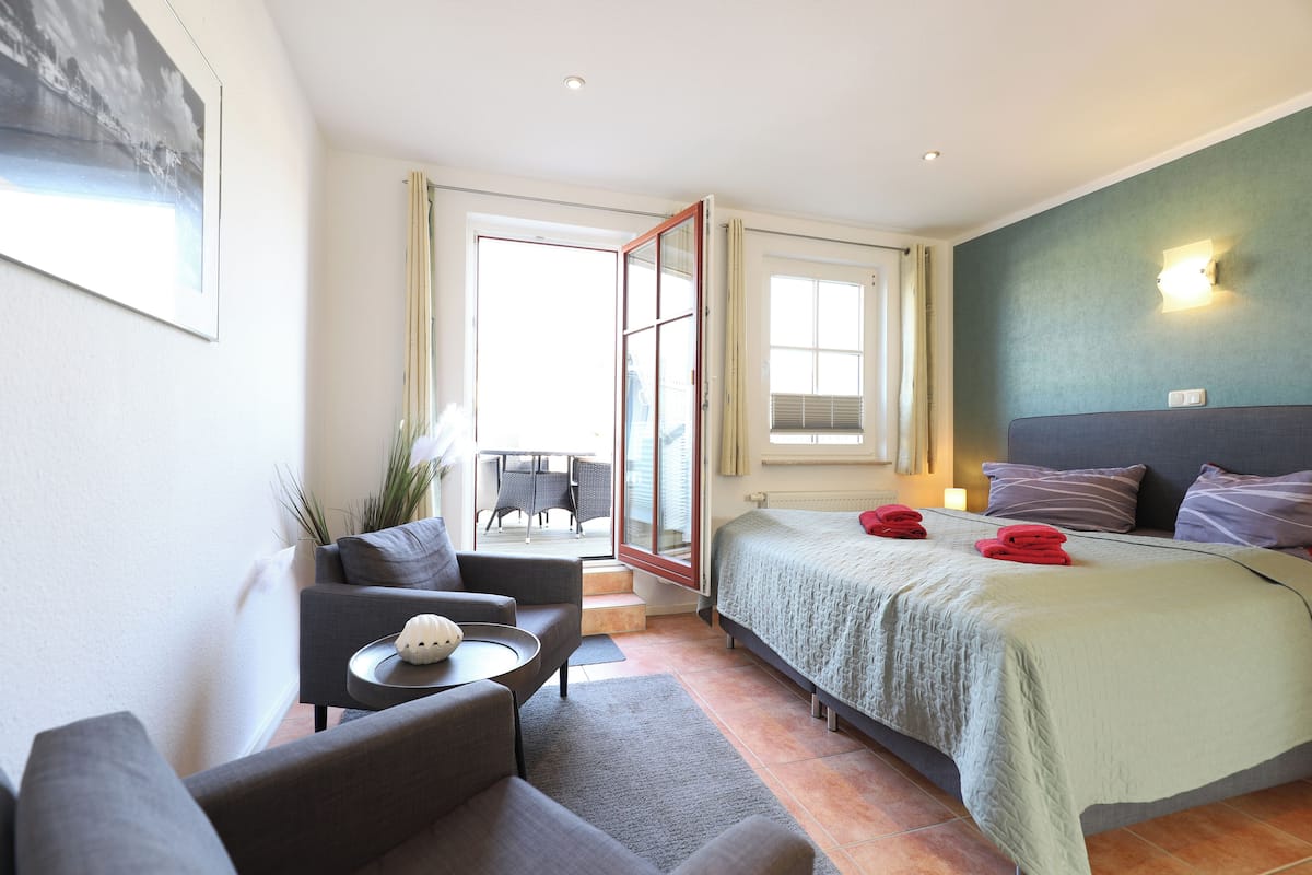 Une chambre d’hôtel avec un lit, un canapé, une petite table, un balcon avec une chaise et une fenêtre.