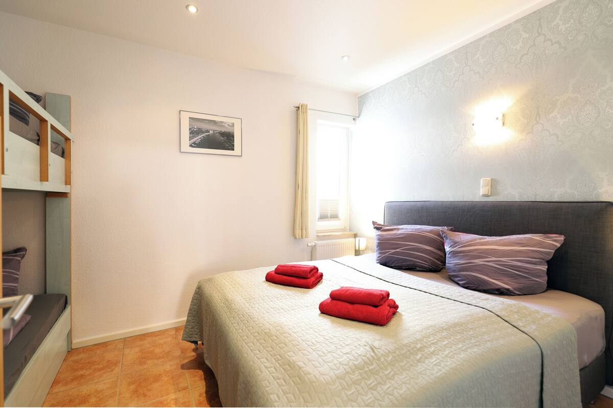 Une chambre à coucher avec un lit, des oreillers, une fenêtre, un radiateur et un tableau accroché au mur.