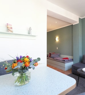 Una sala de estar moderna con un sofá, una mesita con un jarrón de flores y una estantería con libros y un objeto decorativo.