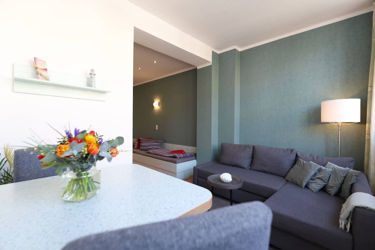Un salon moderne avec un canapé gris, une petite table ronde et un vase de fleurs posé sur une table blanche.