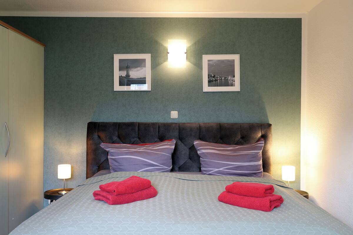 Une chambre d’hôtel avec un grand lit, deux cadres photos accrochés au mur et des lampes de chevet.