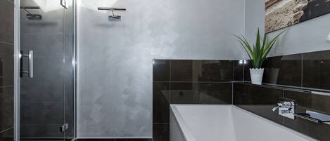 Un baño moderno con cabina de ducha de vidrio, una bañera amplia y una planta en maceta.