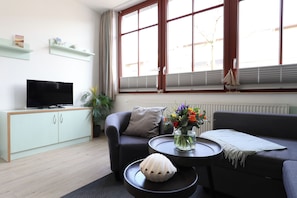 Una sala de estar moderna con un sofá, una mesa de centro, un televisor y una ventana con persianas.
