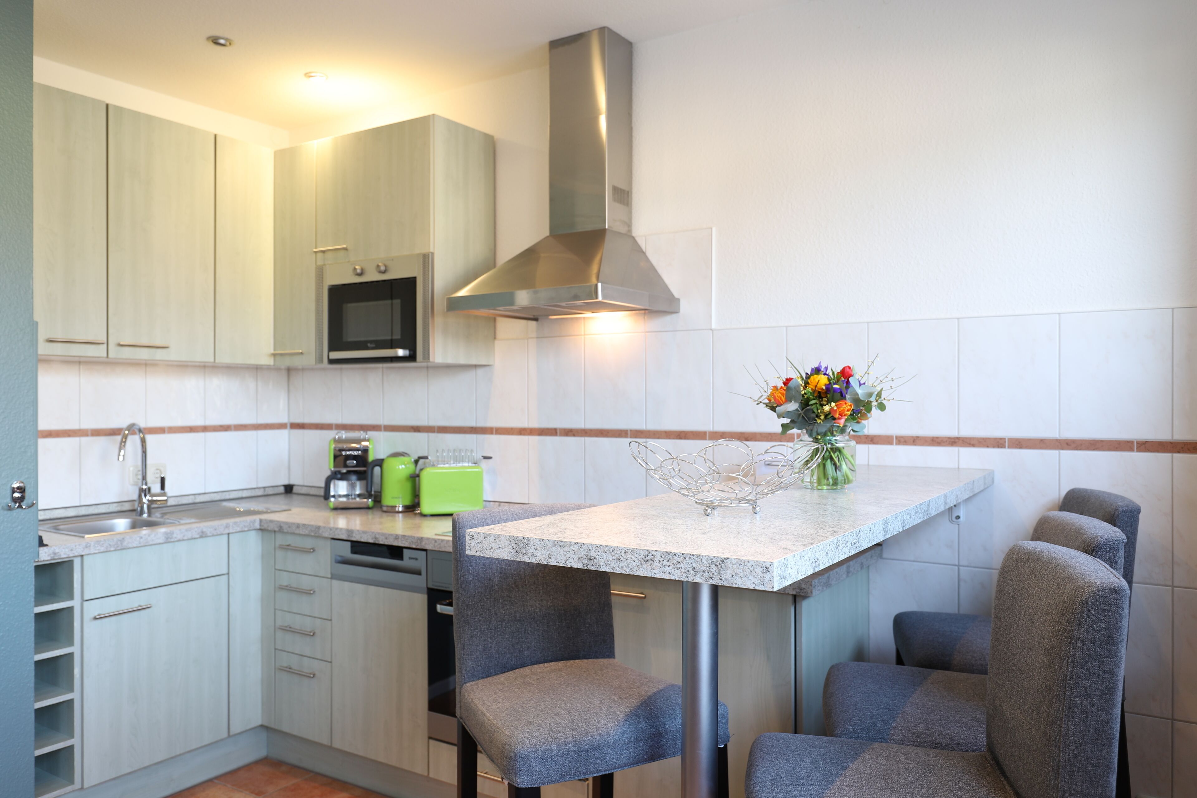 A modern kitchen with a built-in oven, microwave, and stainless steel range hood. There is a small dining area with a table and four chairs.