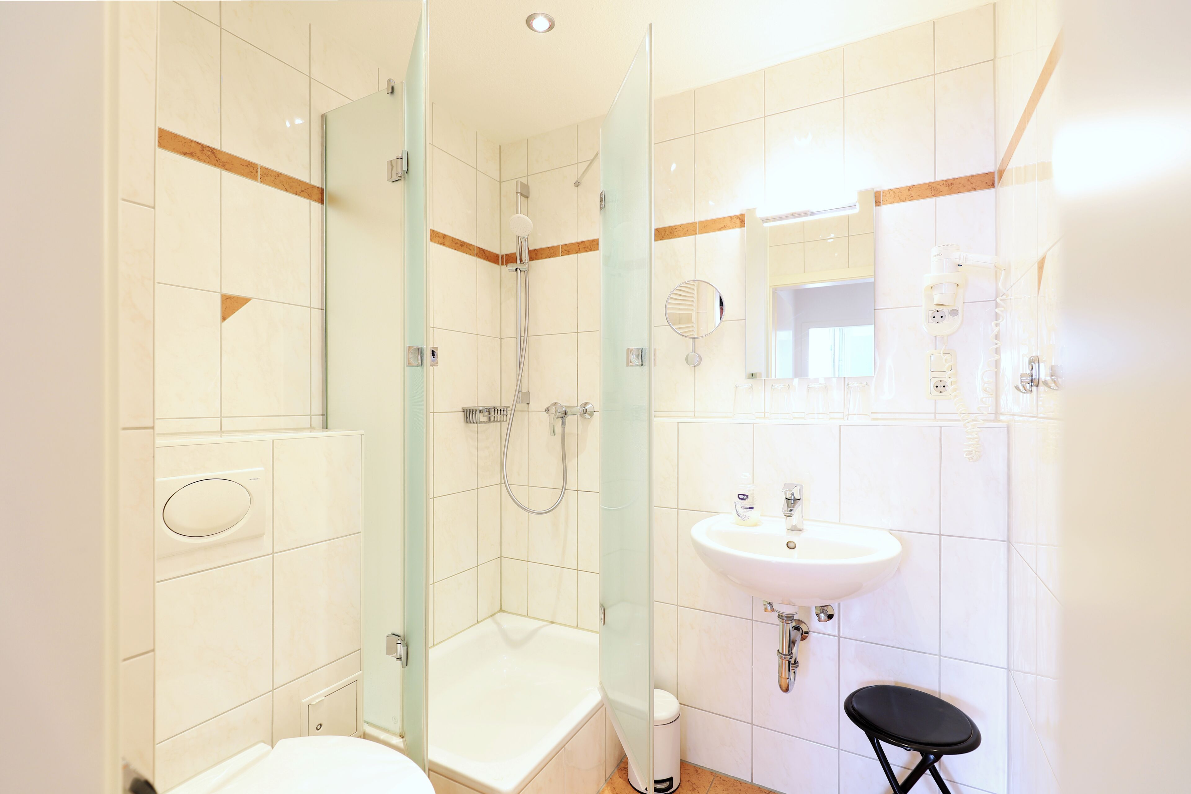 Un bagno con doccia vetrata, lavandino bianco e un piccolo sgabello.