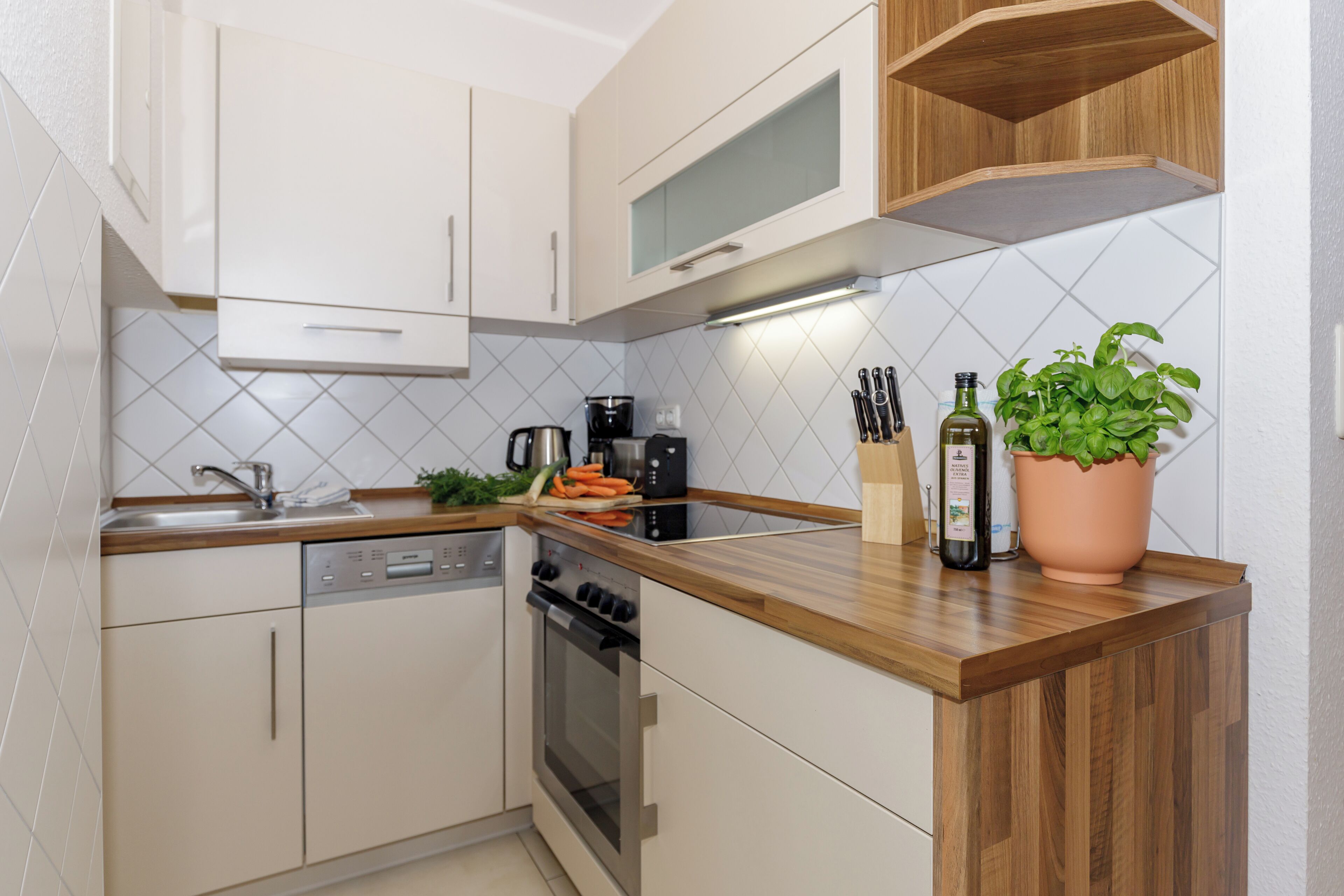 Une cuisine moderne avec des meubles blancs, un plan de travail en bois, un lave-vaisselle, un four et un pot de basilic.